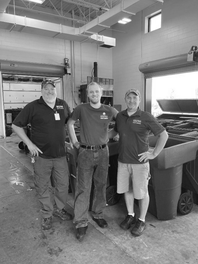 Three men standing in front of trash bins.