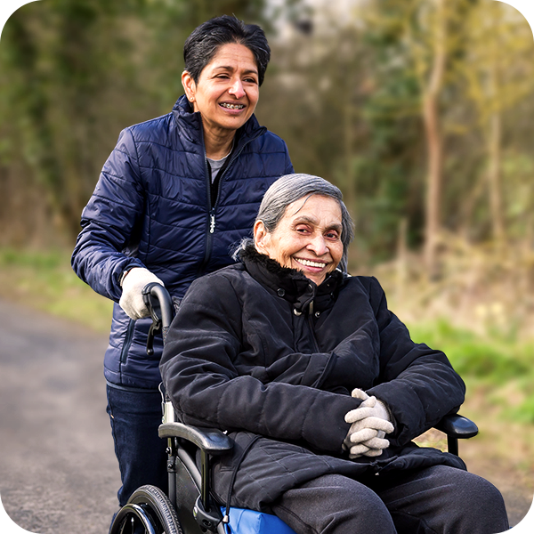 A woman assisting an older man in a wheelchair, both smiling, as part of the Tribal Care services.